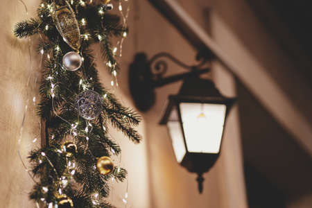 Stylish christmas spruce branches with ornaments and lights illumination on old building in evening. Atmospheric magic time. Christmas festive decor for winter holidays. Merry Christmas!の写真素材