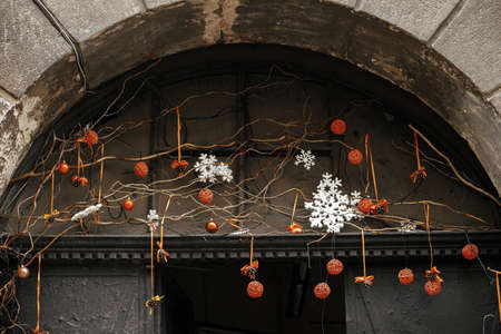 Stylish simple christmas decoration with branches and orange ornaments on window or door. Christmas festive street decor for winter holidays in european city street. Merry Christmas!の写真素材