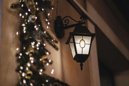 Stylish christmas lantern and spruce branches lights illumination on old building in evening. Atmospheric magic time. Christmas festive decor for winter holidays. Merry Christmas!の写真素材