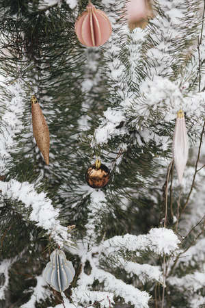 Modern christmas ornaments hanging on snowy pine tree branch. Decorated christmas tree with stylish baubles in snow outdoors. Winter holidays in countryside. Merry Christmas! Space for textの写真素材