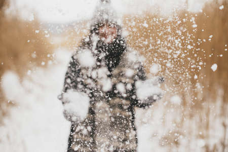Snow in air on background of blurred image of stylish happy woman  in knitted gloves in winter park....