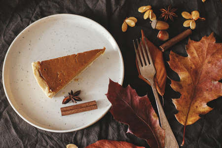 Pumpkin pie slice on modern plate on rustic table with linen napkin, autumn flowers and leaves, anise and cinnamon. Top view. Happy Thanksgiving. Homemade pumpkin tart recipeの写真素材