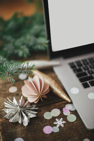 Stylish christmas ornaments and decorations on background of laptop with blank screen on rustic...