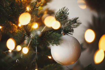 Modern christmas tree ornaments, white baubles and golden christmas lights bokeh close up. Space for...
