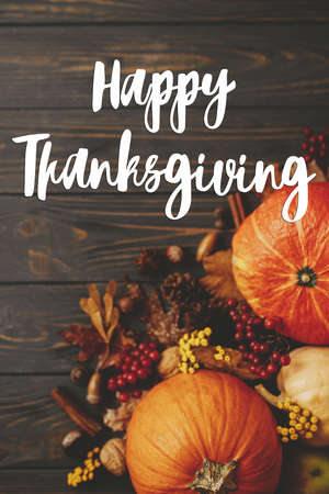 Happy Thanksgiving Card. Happy thanksgiving text on pumpkins, autumn leaves, anise, berries, acorns border on rustic wood flat lay. Season's greetings, handwritten lettering. Give thanksの写真素材
