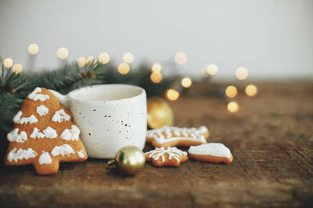 Christmas gingerbread cookies, coffee cup, fir branches on background of warm lights bokeh on rustic...