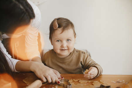 Adorable little daughter and mother making together gingerbread cookies on messy wooden table in modern room. Cute toddler girl helps making christmas cookies. Mommy daughter lovely momentsの写真素材