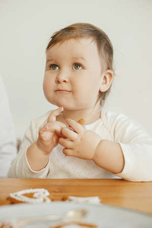Cute little girl eating christmas gingerbread cookies with icing on wooden table. Happy family time together, authentic lovely moments. Xmas holiday preparations. Adorable helper toddlerの写真素材