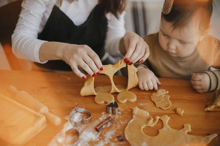 Adorable little daughter and mother making together gingerbread cookies on messy wooden table in modern room. Cute toddler girl helps making christmas cookies. Mommy daughter lovely momentsの写真素材