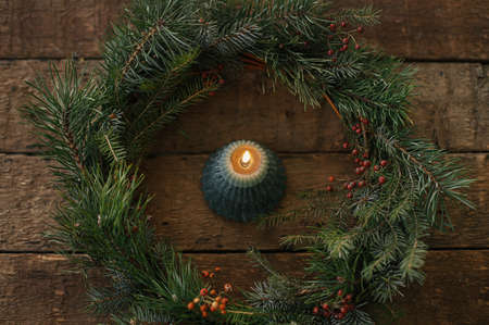 Stylish burning candle in rustic christmas wreath on old wooden background, top view. Christmas advent. Moody atmospheric time. Merry Christmas and Happy holidays! Modern xmas tree candleの写真素材