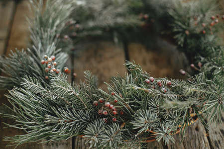 Stylish christmas wreath with pine and fir branches and red berries in snow on rustic old wooden background close up. Happy holidays. Rustic xmas wreath. Winter holidays in countrysideの写真素材