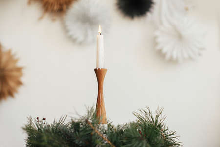 Stylish burning candle in rustic christmas wreath on wooden table on background of paper swedish stars on wall. Christmas advent. Moody atmospheric time. Merry Christmas and Happy holidays!の写真素材