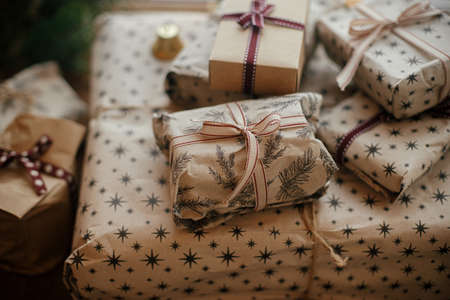 Stylish christmas gifts wrapped in craft paper, fir branches and bells on rustic wood. Stylish scandinavian xmas presents, atmospheric winter time in countryside. Merry Christmas!の写真素材