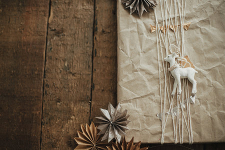 Stylish christmas gift wrapped in craft paper with reindeer toy and swedish paper stars on rustic wood. Flat lay with space for text. Stylish scandinavian xmas presents. Merry Christmas!の写真素材