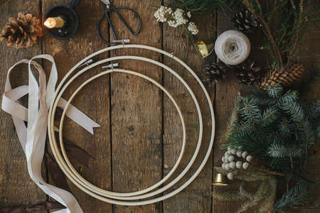 Making modern christmas wreath, rustic flat lay. Fir branches, brunia herb, ribbons, round wooden hoops, scissors, thread on rustic table. Atmospheric image. Winter holidays preparationの写真素材