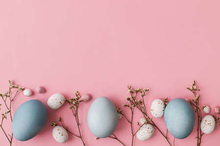 Happy Easter! Easter eggs and flowers flat lay on pink background with space for text. Modern natural dyed blue easter eggs and white flowers on pink. Greeting card templateの写真素材