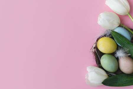 Stylish easter eggs in nest and flowers flat lay on pink background. Natural dyed colorful eggs, feathers nest and tulips. Greeting card template, easter background. Space for textの写真素材