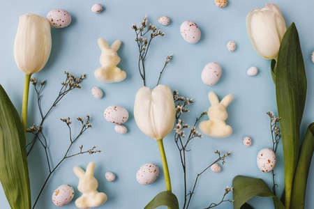 Stylish easter eggs, tulips and bunnies composition flat lay on blue background. Modern chocolate...
