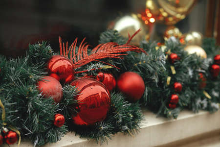Stylish christmas spruce branches and red and gold baubles decoration on window of building or shop....