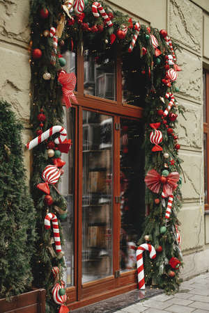 Stylish christmas candy cane, red ornaments, spruce branches decoration on window or door of building or shop. Christmas festive  decor for winter holidays in city street. Merry Christmas!の写真素材