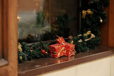 Stylish christmas spruce branches, red gifts, gold baubles decoration on window of building or shop. Christmas festive  decor for winter holidays in european city street. Merry Christmas!の写真素材