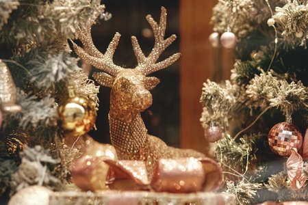 Stylish golden reindeer and modern christmas tree with glitter baubles in window, fairytale decoration. Atmospheric magic time. Christmas festive decor for winter holidays. Merry Christmas!の写真素材