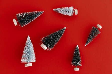 Christmas flat lay. Stylish little christmas trees composition on red background. Modern minimalist...