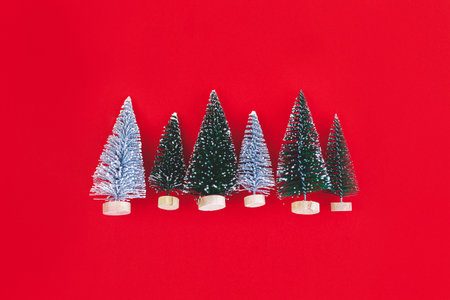 Merry Christmas and Happy New Year! Stylish little christmas trees on red background flat lay. Modern minimalist greeting card with space for text. Minimal xmas flat layの写真素材