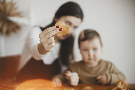 Lovely mommy daughter moments, happy family. Mother holding heart shaped cookie close up, making together with little daughter christmas gingerbread cookies. Holiday preparationsの写真素材