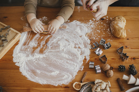 Adorable baby daughter kneading dough together with mother for gingerbread cookies, hands close up. Messy festive table top view. Cute toddler girl helps making christmas cookies. Authentic momentsの写真素材