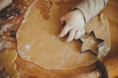 Cute little girl making christmas cookies on messy table, close up. Adorable toddler daughter helping mother and cutting dough for gingerbread cookies. Lovely moments, holiday preparationsの写真素材