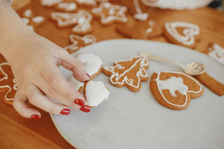 Woman hand holding christmas gingerbread cookie with icing on wooden table, close up.  Decorated baked christmas cookies with sugar frosting. Xmas holiday preparationsの写真素材