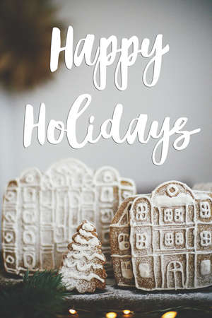 Happy Holidays text on christmas gingerbread cookie houses and trees with golden lights on rustic...