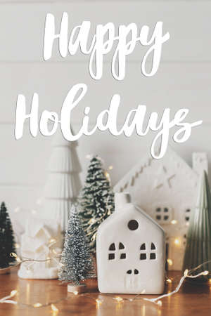 Happy Holidays text on festive christmas scene, miniature holiday village. Stylish Christmas trees and little houses. Season's greetings card. Handwritten sign. Merry Christmas!の写真素材