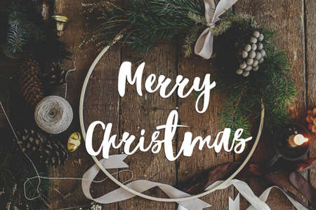 Merry Christmas greeting card. Merry Christmas text on christmas wreath flat lay on rustic table....