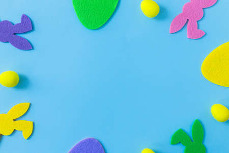 Colorful Easter bunnies and eggs frame on blue background, flat lay with space for text. Happy...
