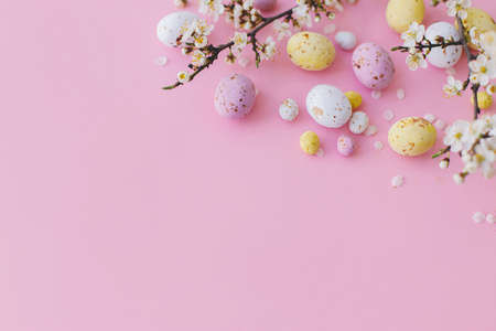 Happy Easter! Colorful Easter chocolate eggs and cherry blossoms border on pink background. Easter flat lay with space for text. Stylish tender spring banner template. Greeting cardの写真素材