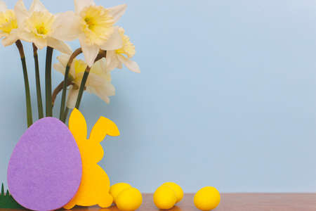Colorful Easter bunnies, eggs and daffodils bouquet on blue background with space for text. Happy Easter! Purple, yellow artificial decor and spring flowers. Easter huntの写真素材