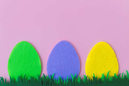 Colorful Easter eggs in grass on pink background, top view with space for text. Happy Easter!...
