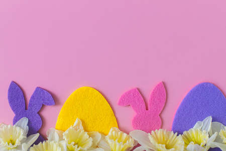 Colorful Easter bunnies, eggs, daffodils border on pink background, flat lay with space for text....