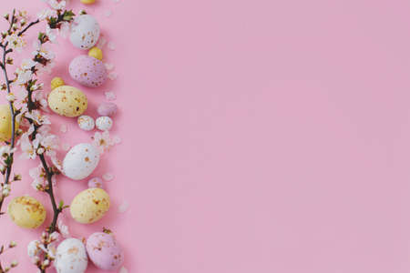Easter flat lay with space for text. Colorful Easter chocolate eggs and cherry blossoms border on...