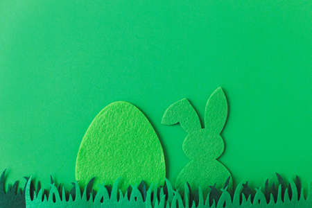 Green Easter egg and bunny in grass on green background, flat lay with space for text. Happy Easter! Green artificial egg and bunny decor. Easter hunt conceptの写真素材