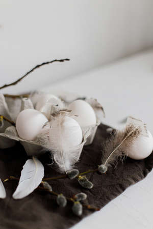 Stylish Easter still life. Natural eggs in tray, feathers, willow branches on rustic linen napkin on...