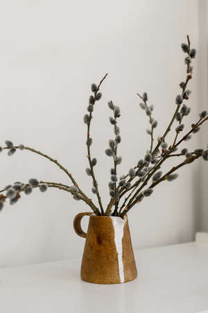 Willow branches in stylish rustic vase on wooden table. Modern Easter still life. Pussy willow branches in home, natural spring decor. Simple Easter rural minimal aesthetics. Space for textの写真素材