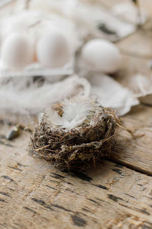 Nest with feathers, willow branches, linen cloth and natural eggs on aged wooden table. Happy Easter! Stylish Easter rustic still life. Simple Easter rural aesthetics.の写真素材