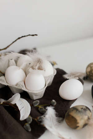 Stylish Easter still life. Natural eggs in tray, feathers, willow branches on rustic linen napkin on...