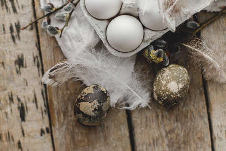 Easter rustic flat lay. Natural eggs in tray, feathers, willow branches, nest on aged wooden table. Stylish Easter rural still life. Simple aesthetics in pastel brown colors. Happy Easterの写真素材