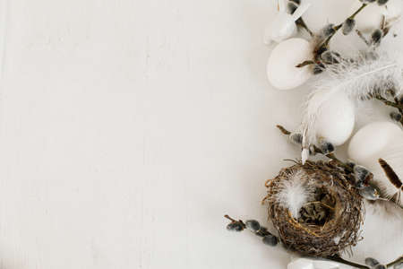 Happy Easter. Natural eggs, feathers, nest, willow branches border composition on white wooden table. Easter rustic flat lay, space for text. Simple stylish easter background and greeting cardの写真素材