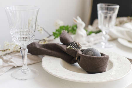 Easter egg in bunny napkin on plate with cutlery, bunny, spring flowers on rustic white table....