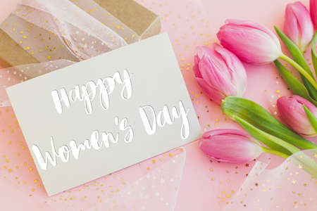 Happy womens day text on greeting card, pink tulips and gift box  on pink background. Stylish...